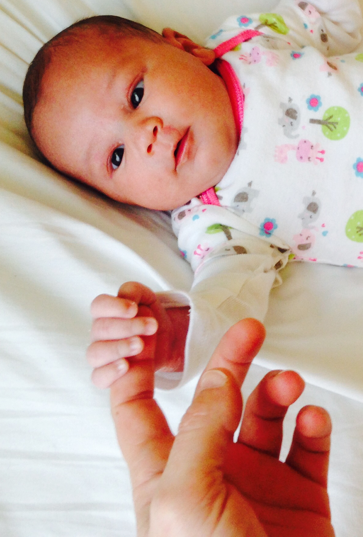 Baby holding the pointer finger of her mother and gazing up at her (mother not pictured)